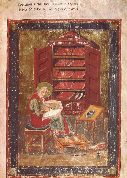 A haloed, white-bearded man in a red tunic sits writing in a large open book next to a tall red cupboard of books, framed in red and blue with a two-line Latin inscription above.