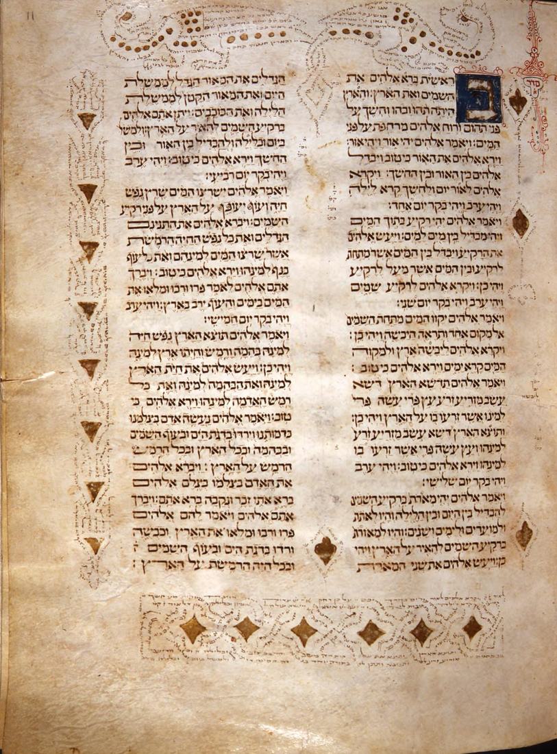 A parchment page of Hebrew text in two columns with a blue decorated initial at the top right, ornamental margin notes in tiny script along the top, left and bottom, and gold diamonds below the text.