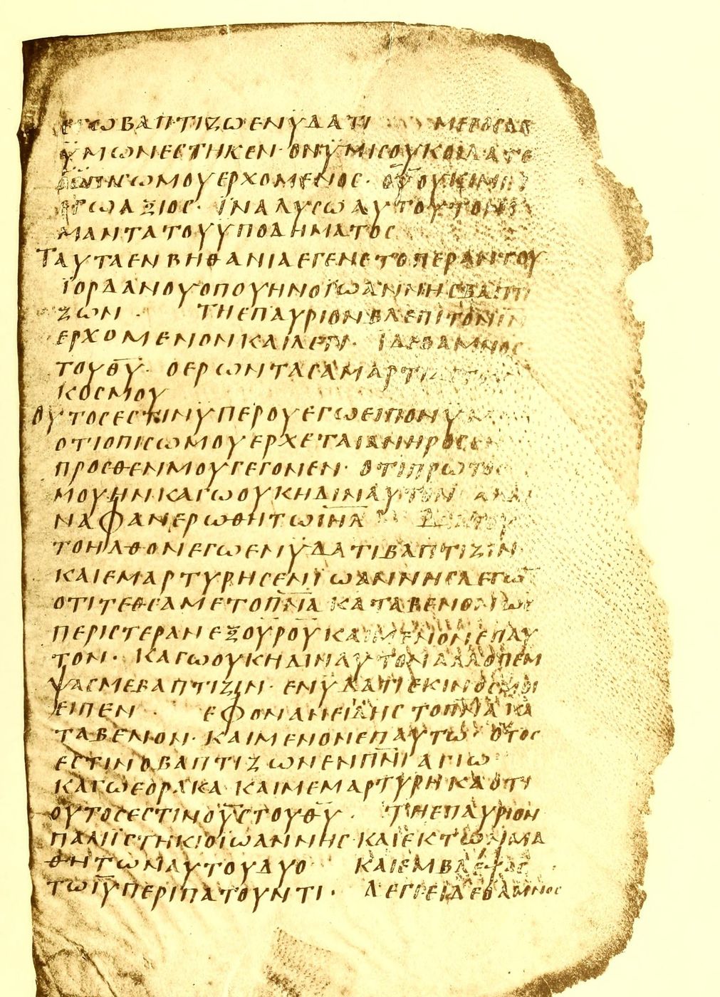 A cream-brown parchment leaf with one column of clear Greek capital letters and ragged right and lower edges.