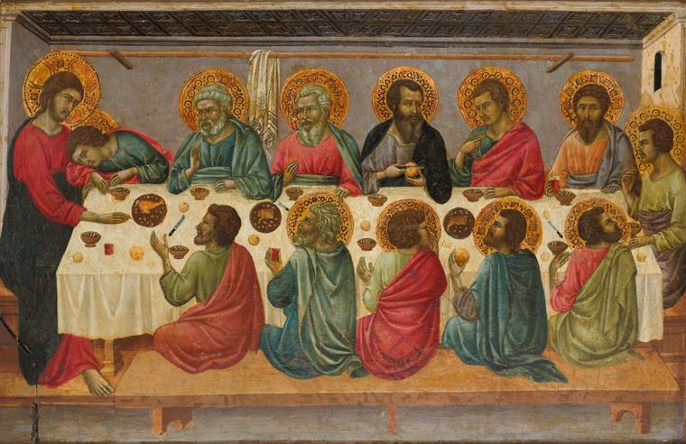 A medieval panel painting of Jesus and the twelve apostles, all with gold halos, around a long white-clothed table set with round loaves, bowls and red cups, under a dark coffered ceiling.