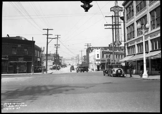 Straßenfoto von 1930 mit Ladenfronten, parkenden Autos und einem abgetragenen Hang.