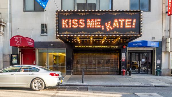 The street-level front of a Midtown Manhattan theatre at number 254, with a lit marquee reading Kiss Me, Kate! above a closed roll-down gate and the words Roundabout Theatre Company at Studio 54 over the entrance, and a parked silver car at the left.