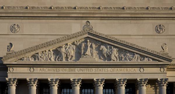 Carved stone pediment with relief sculpture above a row of Corinthian columns, with the inscription Archives of the United States of America, lit by warm evening light.