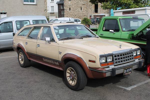 A tan station wagon with brown lower-body panels, "Eagle" lettering on its boxy grille and "Elegance 4x4" lettering on the lower door, parked on a paved lot beside a silver van and a green pickup truck.