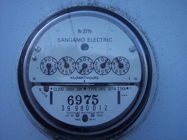 A round glass-covered electric meter showing five small dials above the word Kilowatthours and a printed number 6975, with the maker's name Sangamo Electric at the top.