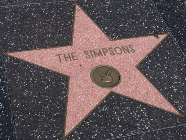 A pink terrazzo star set in dark speckled pavement, with the words THE SIMPSONS in brass letters and a brass television emblem at its center.