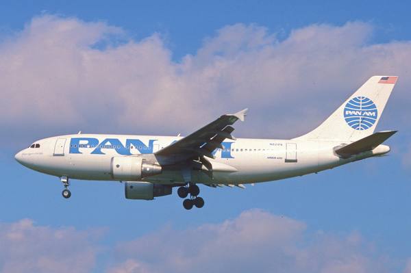 A white Pan Am Airbus A310 with blue lettering and the Pan Am globe on its tail, landing gear down, flying against a blue sky with pink-tinged clouds.