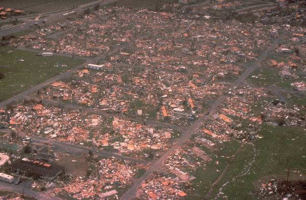 An aerial view of a neighbourhood where houses have been flattened or had their roofs torn off, with debris spread across the lots and streets.