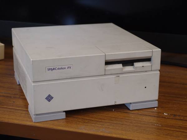 A cream-colored, flat Sun SPARCstation IPX workstation case with a floppy drive slot, a SPARCstation IPX label and a Sun logo, sitting on a wooden table.