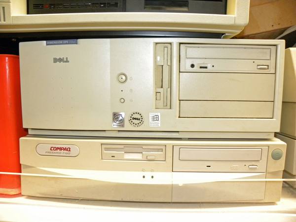 Two beige desktop computer cases stacked on a shelf: a Dell Dimension XPS D266 above a Compaq Presario 7150, each with a floppy drive and a CD-ROM drive, and the Dell with Intel Pentium II, Dell and Designed for Windows stickers on its front.
