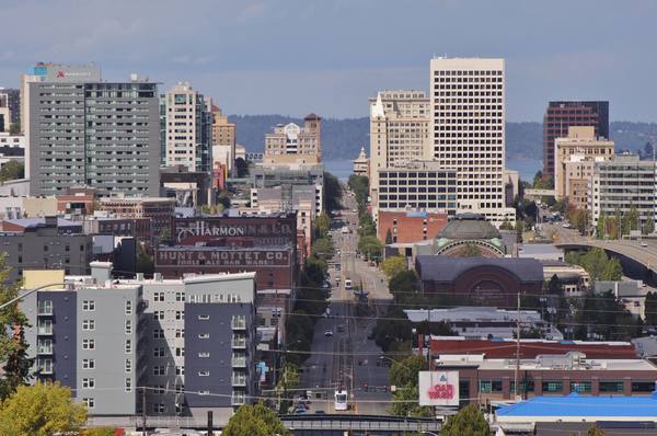 A view down a long city street toward a cluster of downtown towers and, beyond them, a stretch of water.