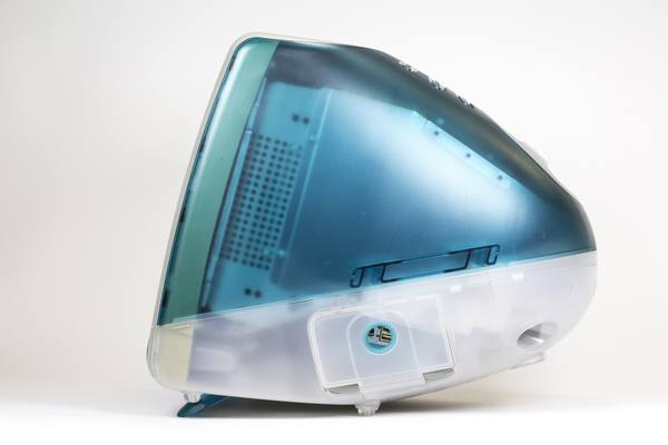 Side view of a translucent blue-green and white all-in-one iMac G3 computer against a pale studio background.