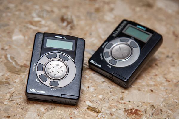 Two black Diamond Rio PMP300 players with small grey LCD screens and round silver control rings, lying on a speckled beige stone surface.