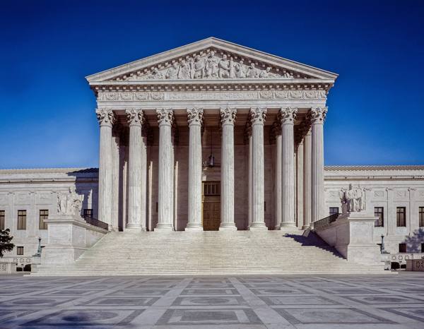 The white marble front of the Supreme Court building under a deep blue sky, with eight tall columns, a sculpted pediment, the words Equal Justice Under Law above the entrance, and a wide flight of steps.
