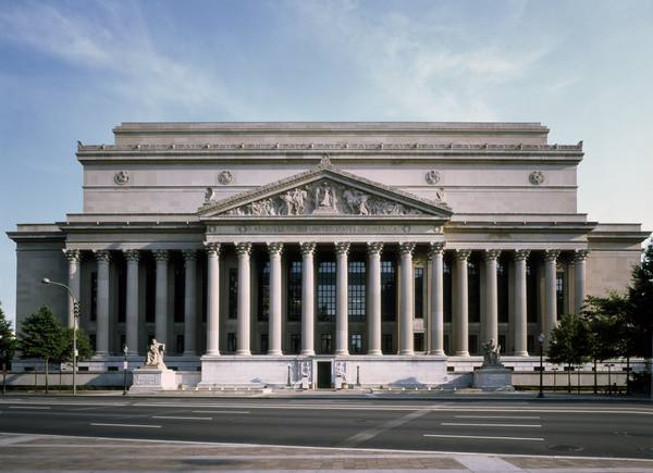 The columned stone front of the National Archives Building in Washington, D.C., with a carved pediment above the words Archives of the United States of America and an empty avenue in front.