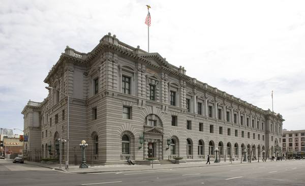 A long gray granite federal courthouse in the Beaux Arts style with an American flag on its roof, seen from a street corner under an overcast sky.