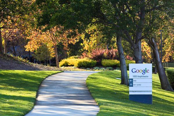 A curving concrete path through a green lawn and autumn trees, with a small Google directional sign at the right.