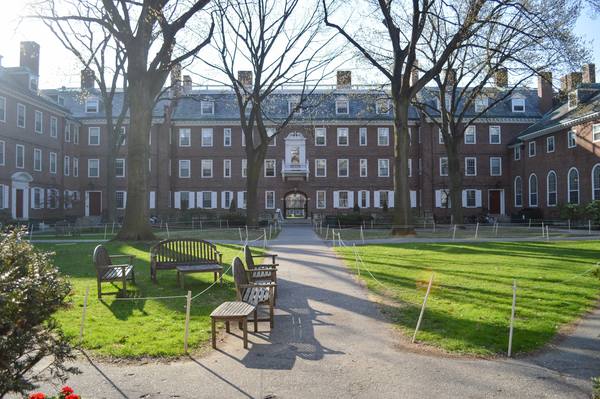 A brick Georgian-style residence hall seen across a green courtyard with a paved path, wooden benches, rope-and-post lawn borders and bare trees.