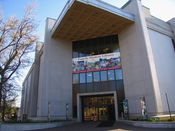 The concrete-and-glass entrance of the Family History Library with a large Find Your Ancestors - Find Yourself banner above the doors and vertical banners by the entrance.