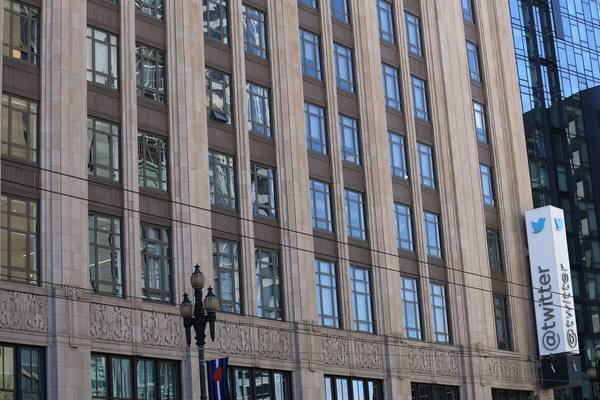 The tan Art Deco facade of a multi-story office building with rows of tall windows, and a white vertical sign with a blue bird logo and the word twitter at the right edge.