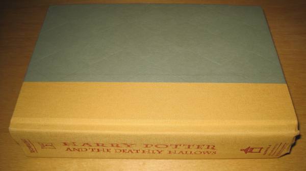 A hardcover book lying flat on a wooden surface, with a plain gray-green cover, a tan cloth spine and the title Harry Potter and the Deathly Hallows in red lettering on the spine.