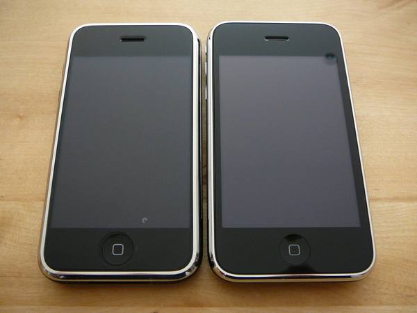 Two black iPhones lying side by side on a light wooden surface, their screens dark.