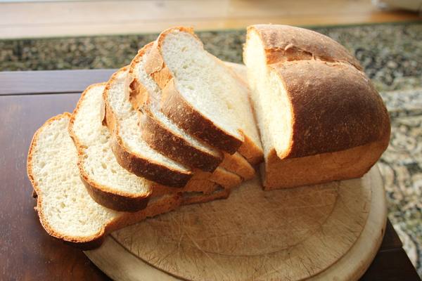 A golden-brown tin loaf of white bread with several slices fanned out in front of it on a round wooden board.