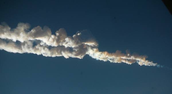 A long, billowing white smoke trail stretching diagonally across a deep blue sky.