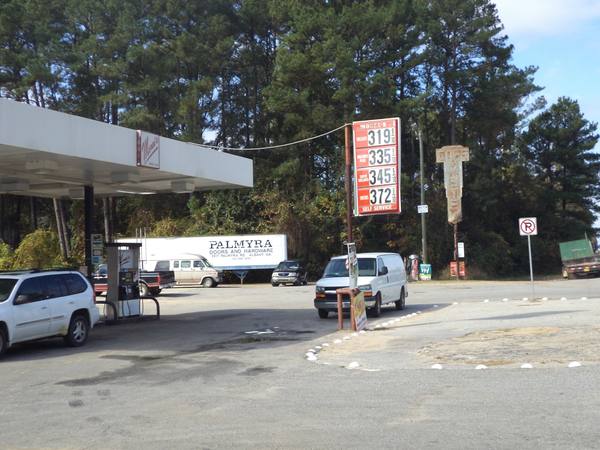A roadside gas price sign listing unleaded at $3.19 9/10, unleaded plus $3.35, super unleaded $3.45 and diesel $3.72, beside a station canopy, a pump and parked vans.