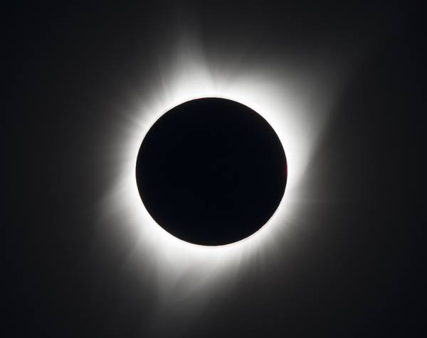 The black disc of the Moon covering the Sun, surrounded by glowing white streamers of the solar corona against a dark sky.