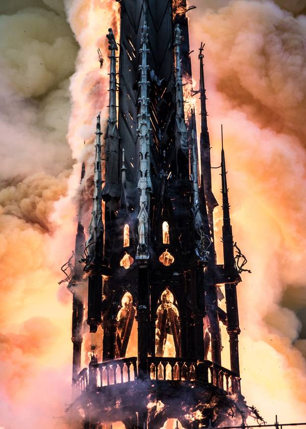 The dark Gothic lattice spire of Notre-Dame, silhouetted and glowing from inside as orange flames and smoke engulf it.